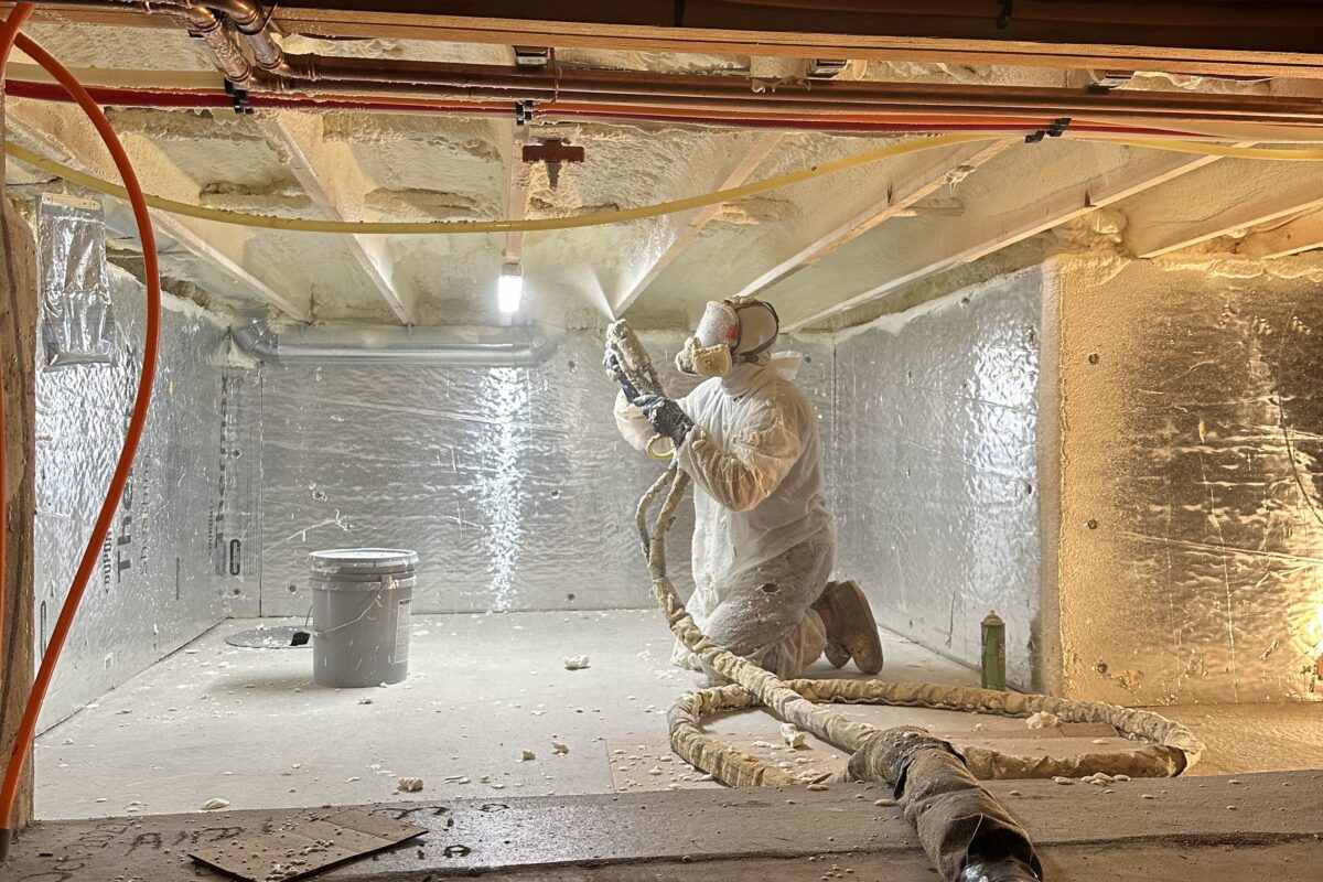 Worker applying insulation in a crawl space renovation